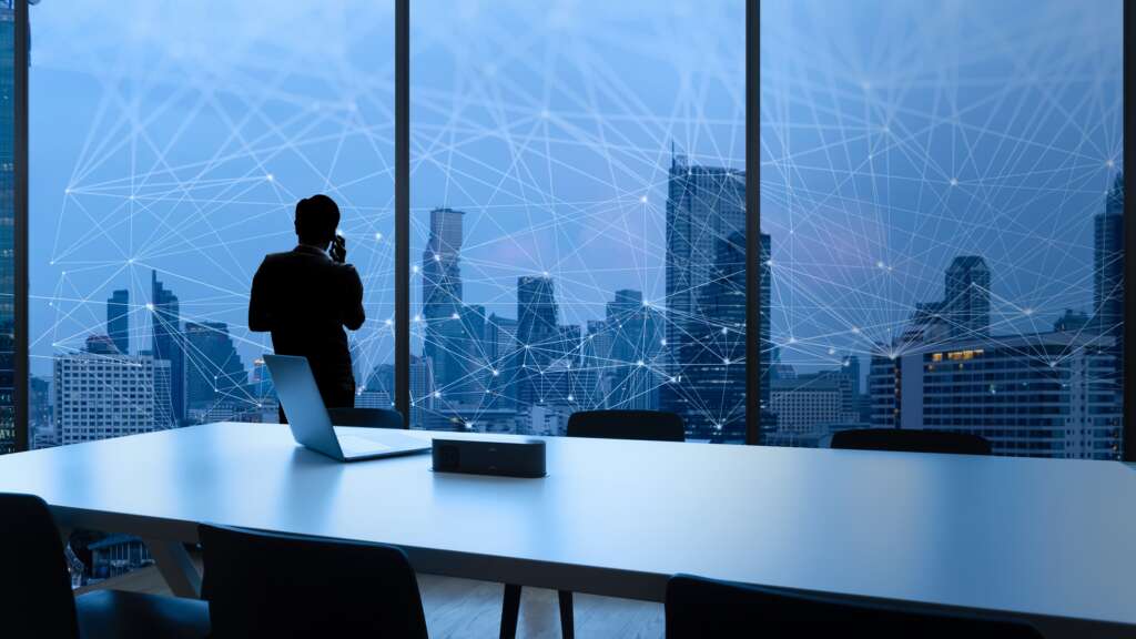 Businessman standing using smart phone and Business Wireless network in office desk and windows and Bangkok city view.